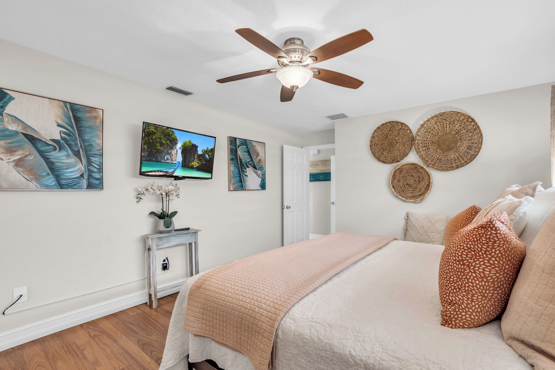 Une chambre à coucher comprenant un lit, un ventilateur de plafond, des œuvres d’art et un téléviseur.