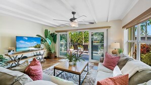 A spacious living room with a large TV, comfortable seating, a ceiling fan, and a view of the outdoor patio area. - Charming Florida Home on the Waterway with Coastal Charm and Easy, Relaxed Vacation Vibes! (Wilton Manors)