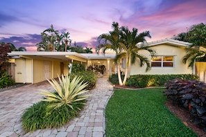 A two-story house with a covered porch, a well-maintained lawn, and various plants. - Charming Florida Home on the Waterway with Coastal Charm and Easy, Relaxed Vacation Vibes! (Wilton Manors)