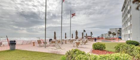 Ett hotell vid stranden med uteservering, en flaggstång med flaggor och utsikt över havet.