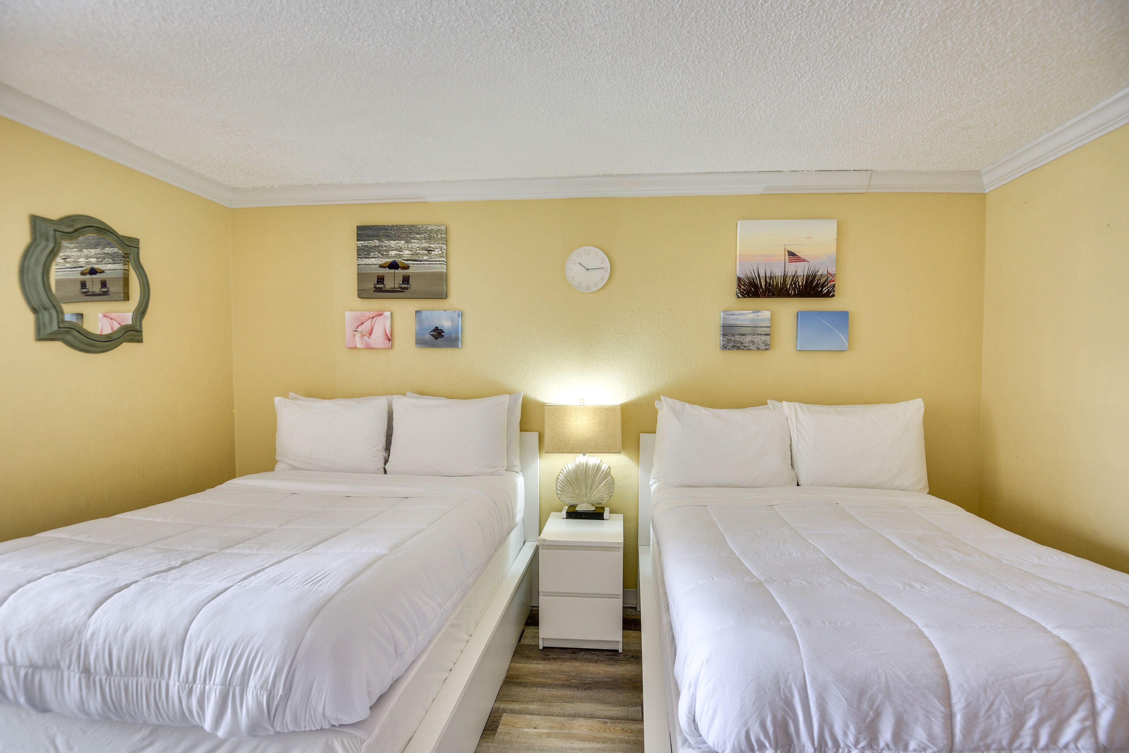 Camera d'albergo con due letti, un comodino con una lampada e opere d'arte alle pareti.