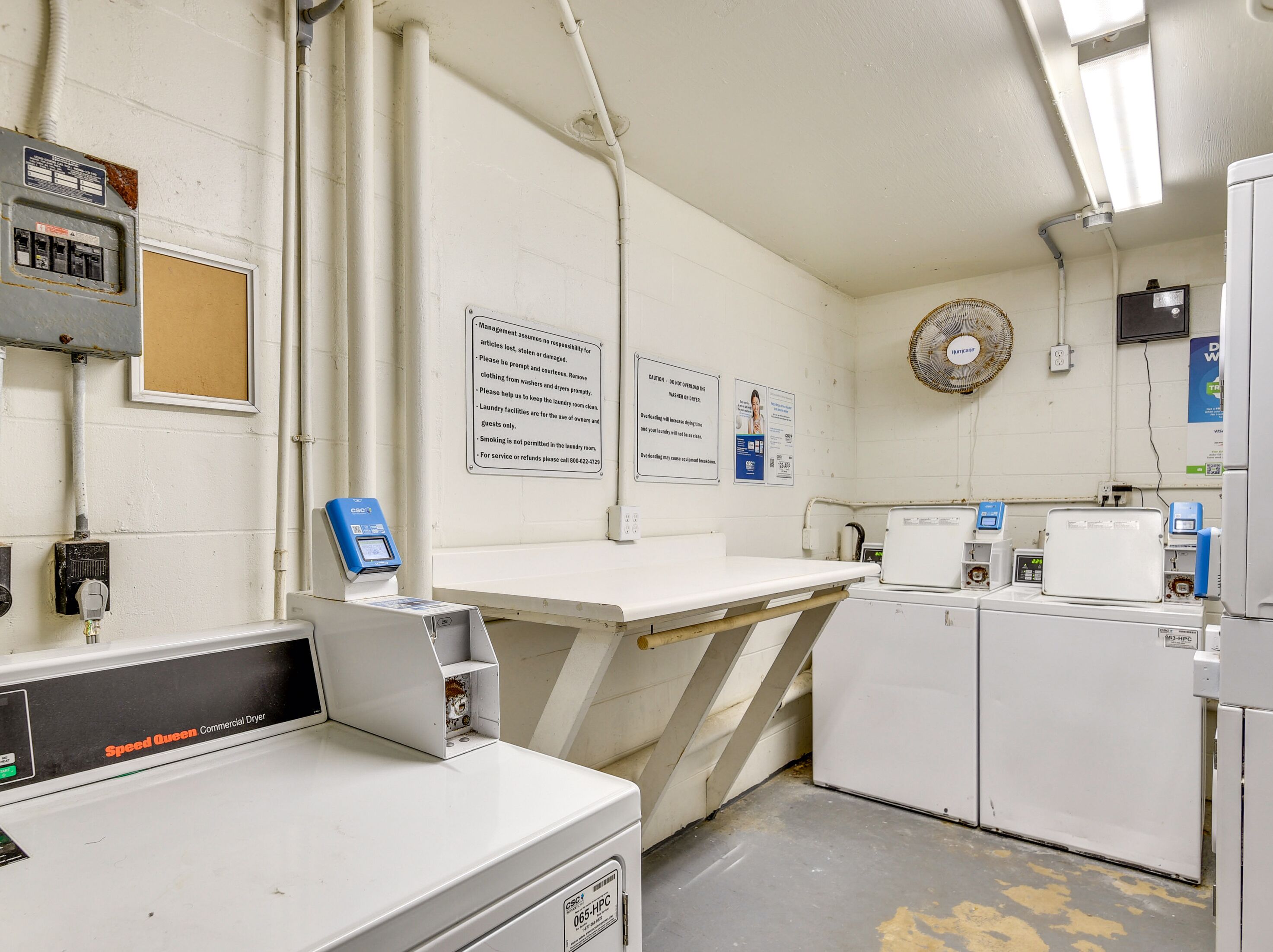 A laundry facility with industrial dryers, control panels, and a fan.