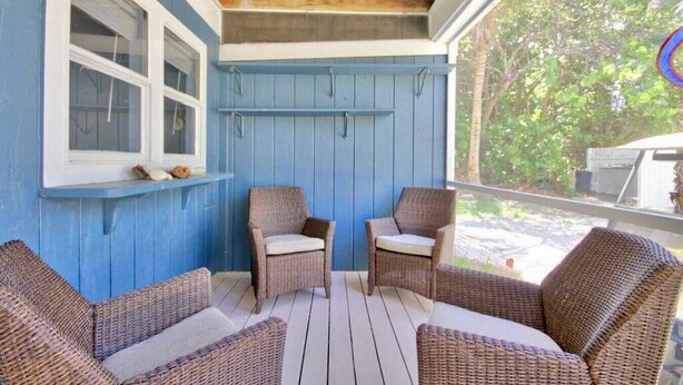 A covered porch with blue walls, two wicker chairs, and a window.