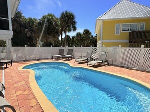A swimming pool with a white fence, lounge chairs, and a yellow building in the background.