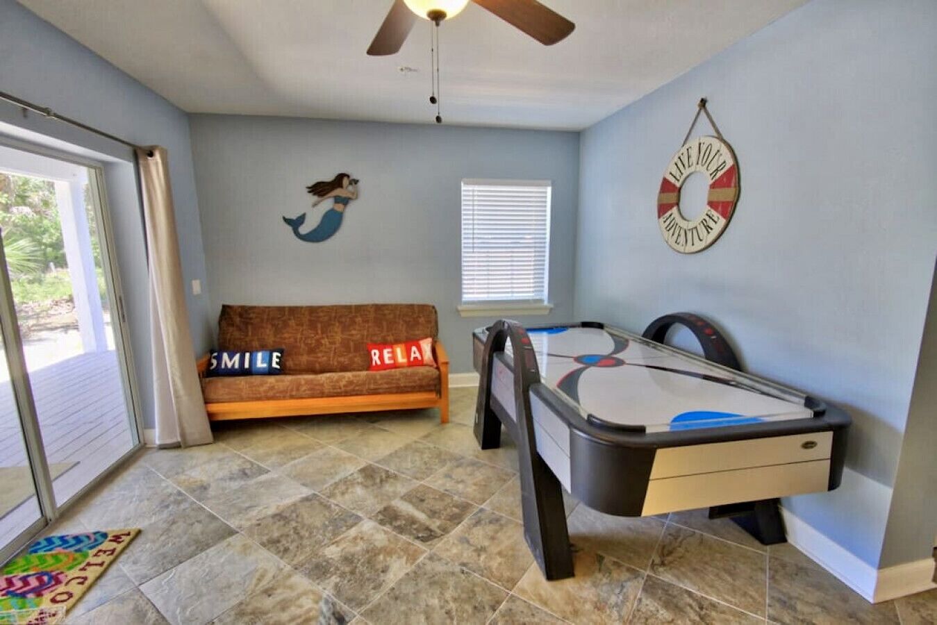 A room with a pool table, a sofa with 'SMILE' and 'RELAX' pillows, a mermaid mural, and a 'LAKE JOY AQUARIUM' sign.