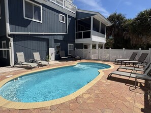 A swimming pool with lounge chairs and a two-story building with balconies.