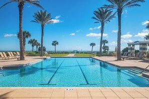 Piscina azul clara con indicador de profundidad de 3 pies, rodeada de palmeras y sillas de descanso, con vista al océano.