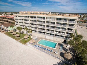 A multi-story hotel with balconies, a swimming pool, and a beach area.