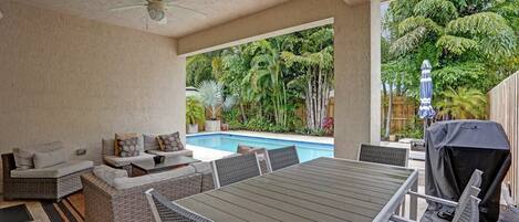 An outdoor patio with a pool, seating area, and grilling station.