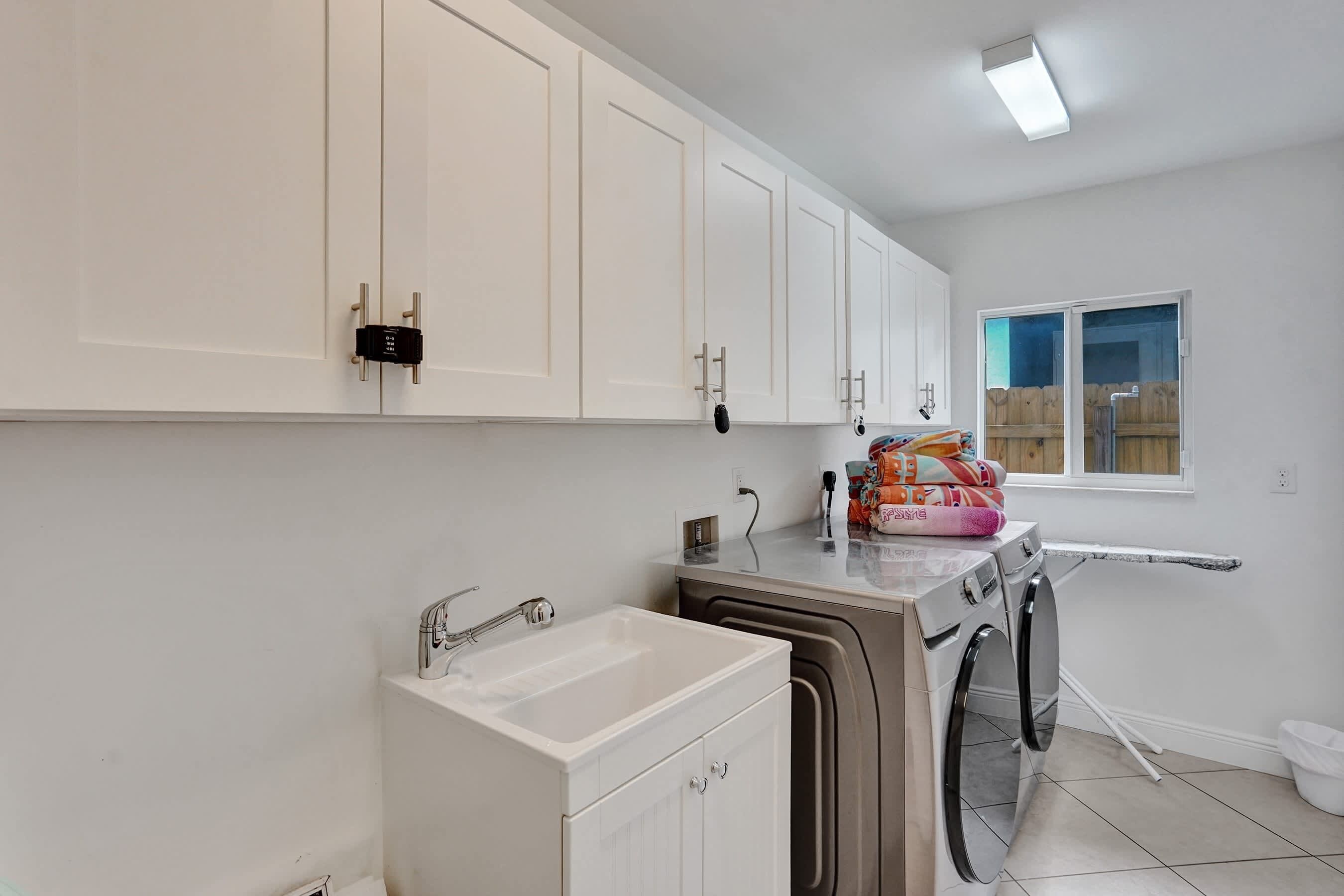 A modern kitchen with white cabinets, a built-in sink, a washing machine, and a window with a view of the outside.