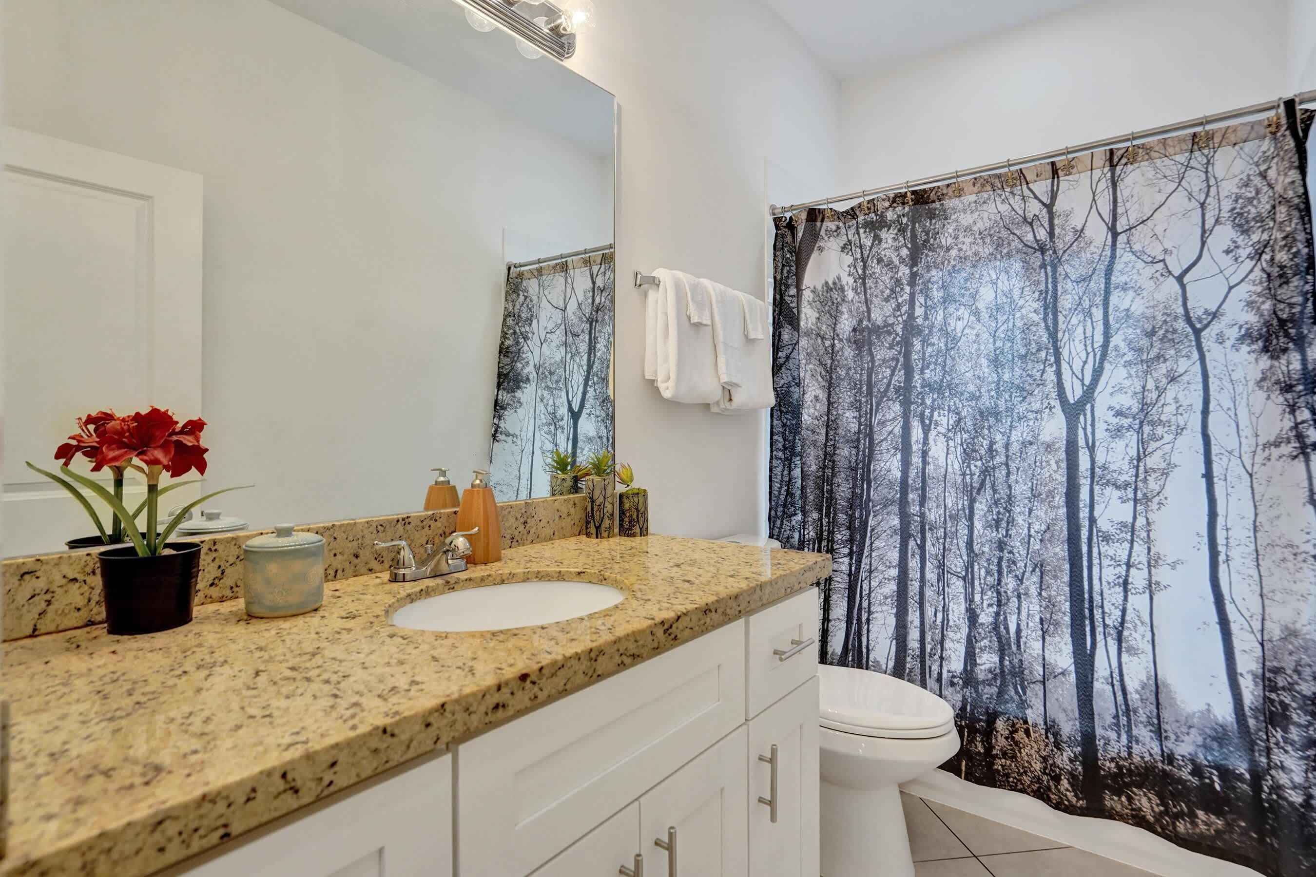 A bathroom with a granite countertop, a sink, a toilet, and a shower curtain with a forest print.