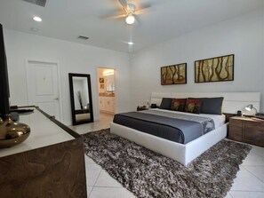 Une chambre à coucher moderne avec un grand lit, un ventilateur de plafond et des œuvres d’art accrochées au mur.