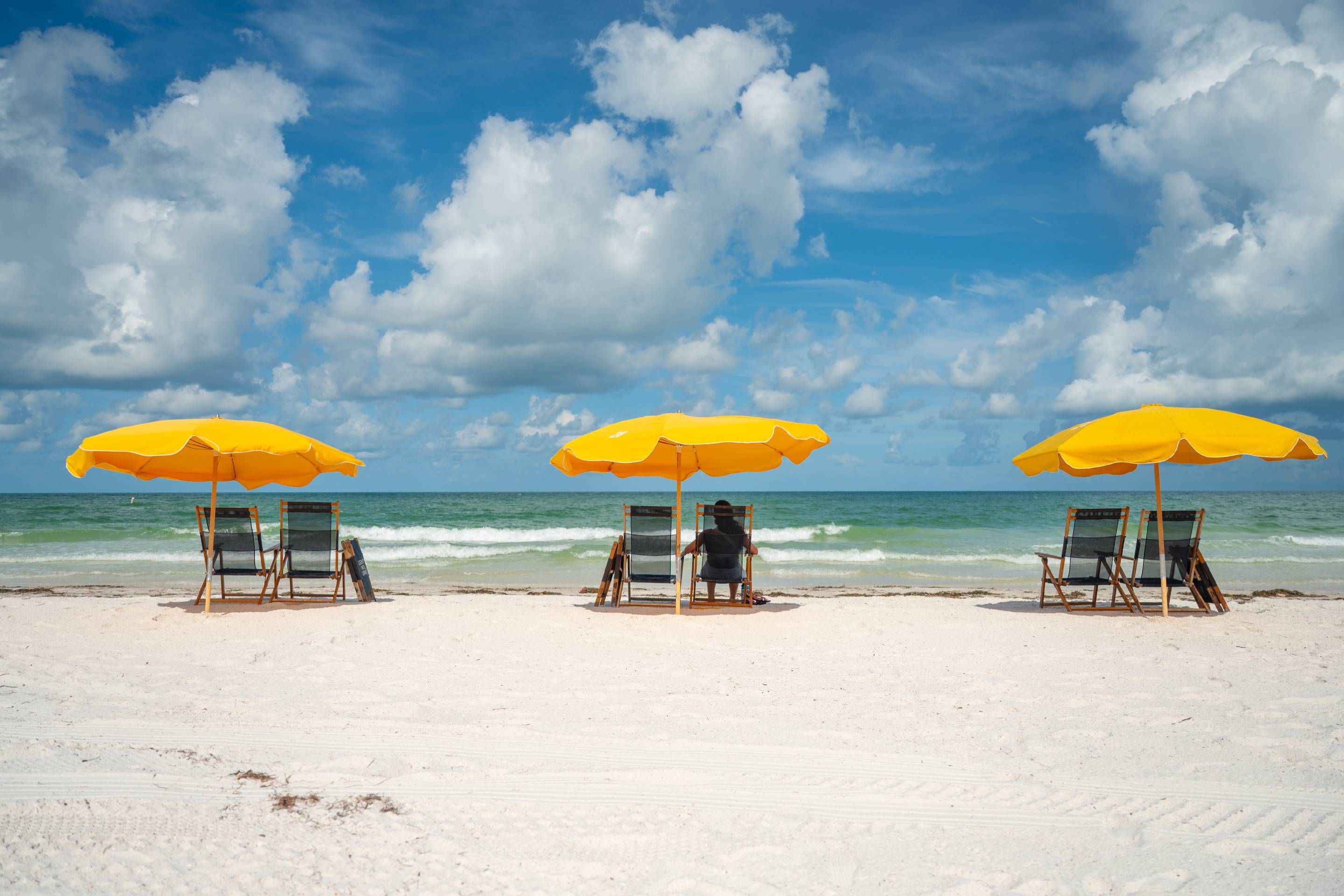 Three beach chairs under yellow umbrellas facing the ocean.