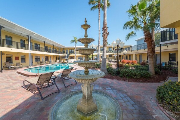 A courtyard with a pool, lounge chairs, and a stone fountain.