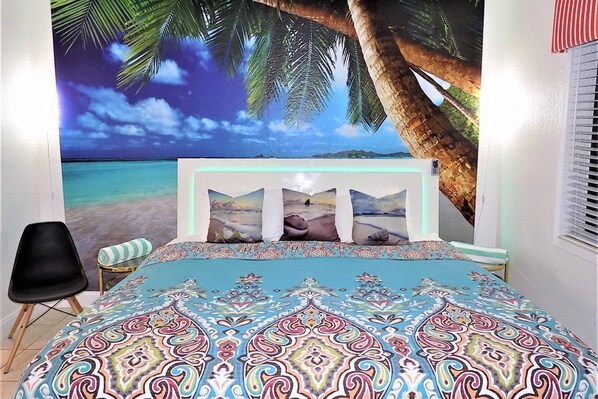 A bedroom with a bed, a chair, and a wall mural of a beach scene.
