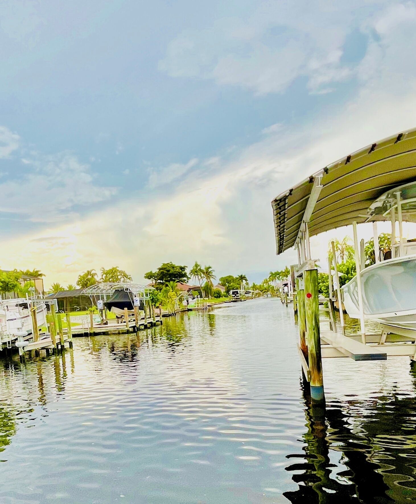 A calm waterway with boats docked on the right, surrounded by greenery and a clear sky.