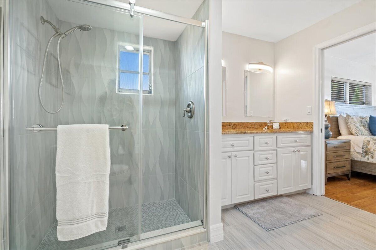 Un baño moderno con cabina de ducha acristalada, una toalla blanca colgada en la puerta y un lavabo con encimera de granito.