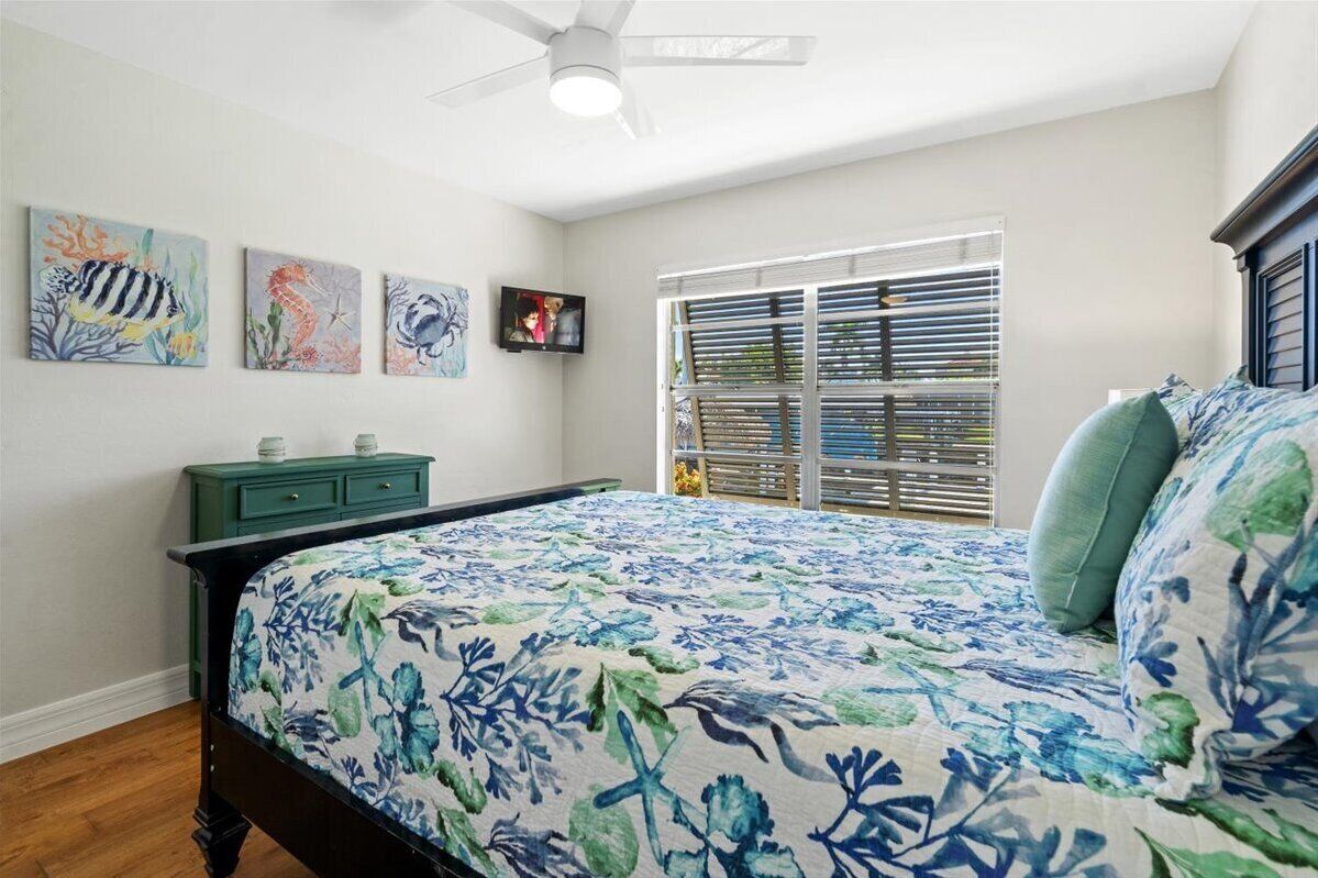 A bedroom with a bed, a green dresser, a ceiling fan, and artwork on the wall.
