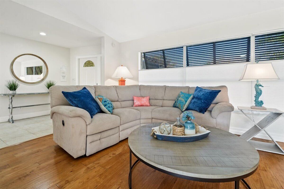 A living room with a beige sectional sofa, two lamps, a round coffee table, and a window with blinds.