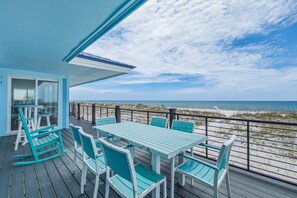 Una terraza con mesa y sillas, con vista a una playa con dunas y el océano.