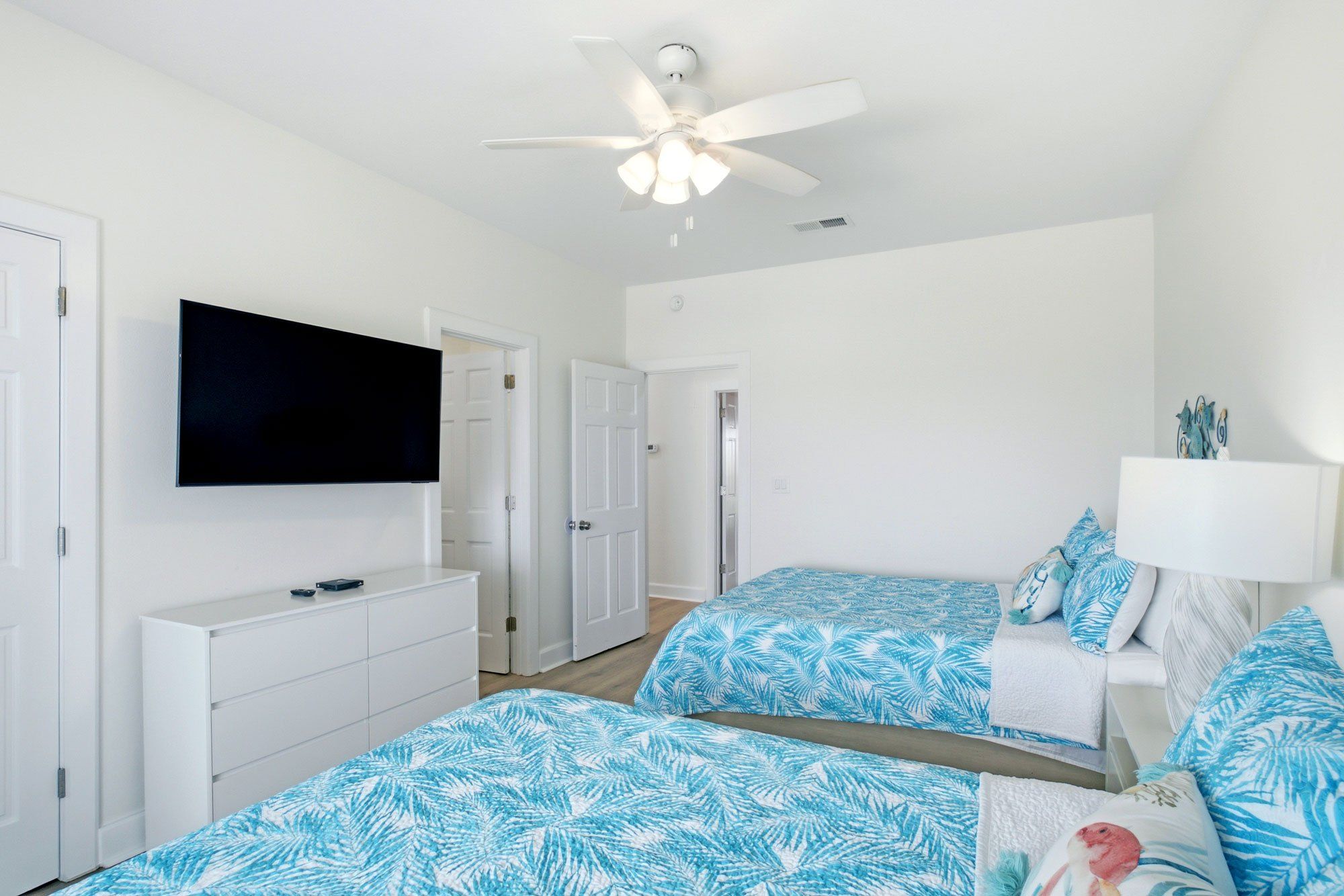 Une chambre avec deux lits, un ventilateur de plafond, une télévision et une commode.