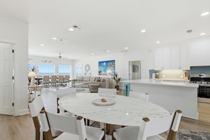 A modern kitchen with white cabinets, a central island, and a dining area with a round table and chairs.