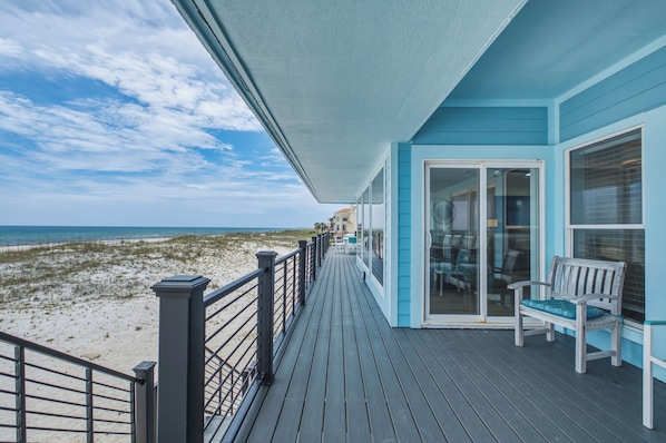 A wooden deck with a glass door leading to a room, overlooking a beach.