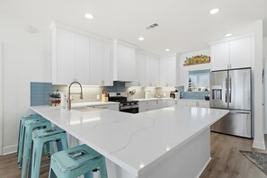 A modern kitchen with white cabinetry, a large island, stainless steel appliances, and teal bar stools.