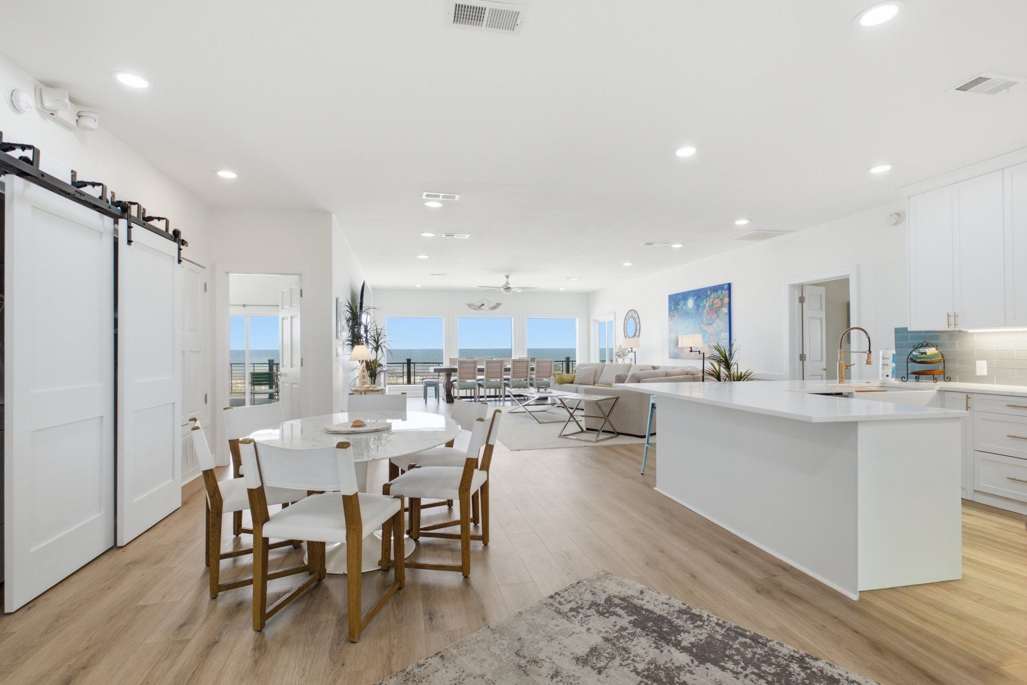 A modern kitchen with white cabinetry, a central island, and a dining area with a round table and chairs.