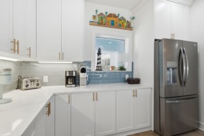 Una cocina moderna con armarios blancos, un refrigerador de acero inoxidable, una cafetera y un tostador.