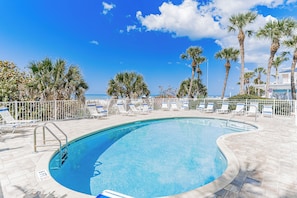 A swimming pool with a view of the ocean, surrounded by palm trees and lounge chairs.