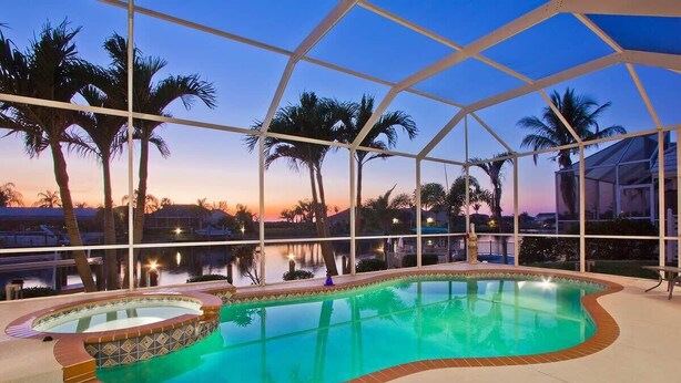 Une piscine intérieure dotée d’une paroi vitrée, entourée de palmiers et offrant une vue sur le coucher de soleil.