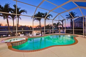 Una piscina interior con cerramiento de vidrio, rodeada de palmeras y vistas al atardecer.