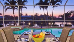 Un espace repas aménagé au bord de la piscine, offrant une vue sur les palmiers et le coucher du soleil.