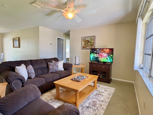 A living room with a brown sofa, a wooden coffee table, a television, and a ceiling fan.