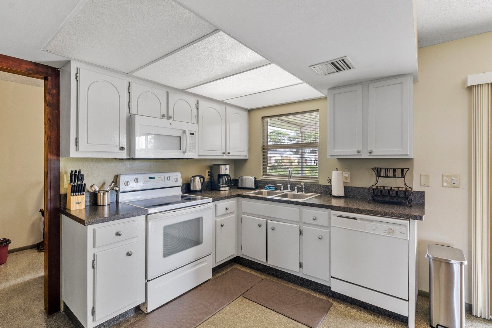A compact kitchen with white cabinets, a stove, a microwave, and a coffee maker.