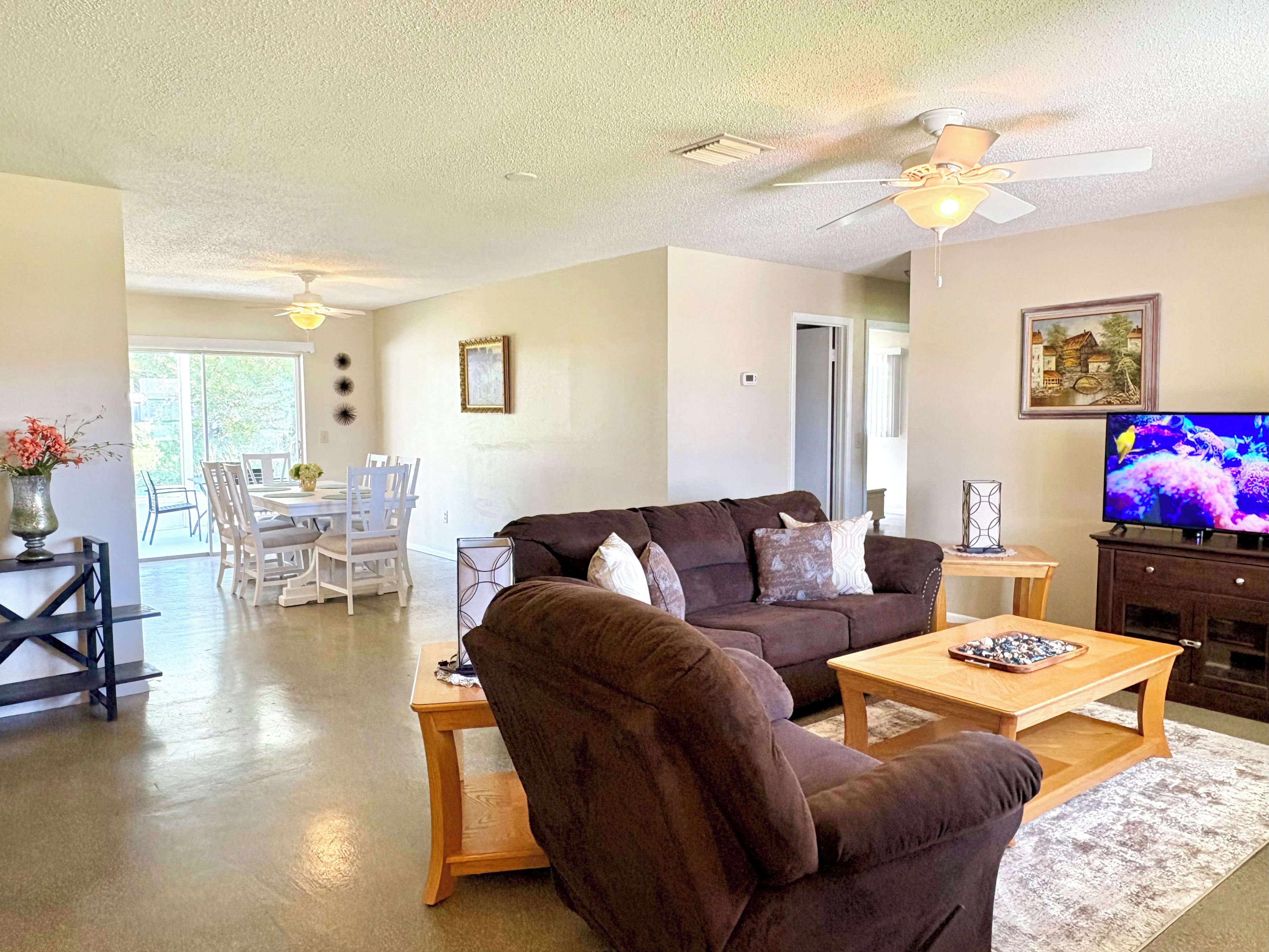 A living room with a brown sofa, a coffee table, and a television. There is a dining area with a white table and chairs.