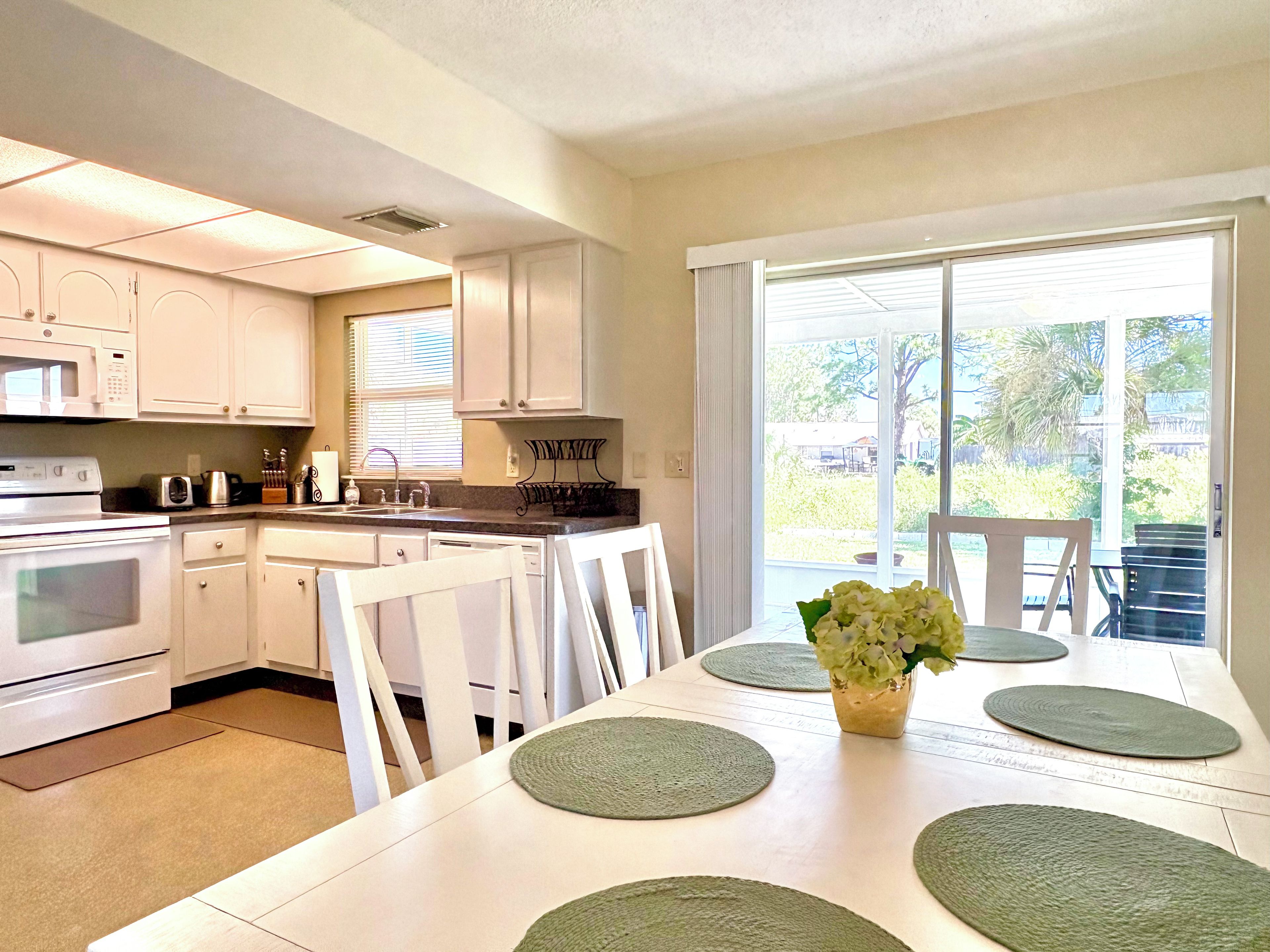 A kitchen with white cabinets, a microwave, and a sink. There is a dining table with chairs and a vase of flowers.