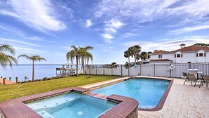 A swimming pool with a view of the sea, surrounded by a fence and palm trees. - Riverfront Titusville Home w/ Pool + Pickleball! (Titusville)