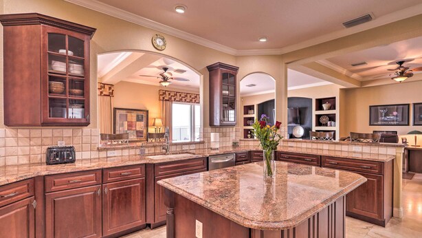 A spacious kitchen with dark wood cabinets, granite countertops, and a central island. - Riverfront Titusville Home w/ Pool + Pickleball! (Titusville)