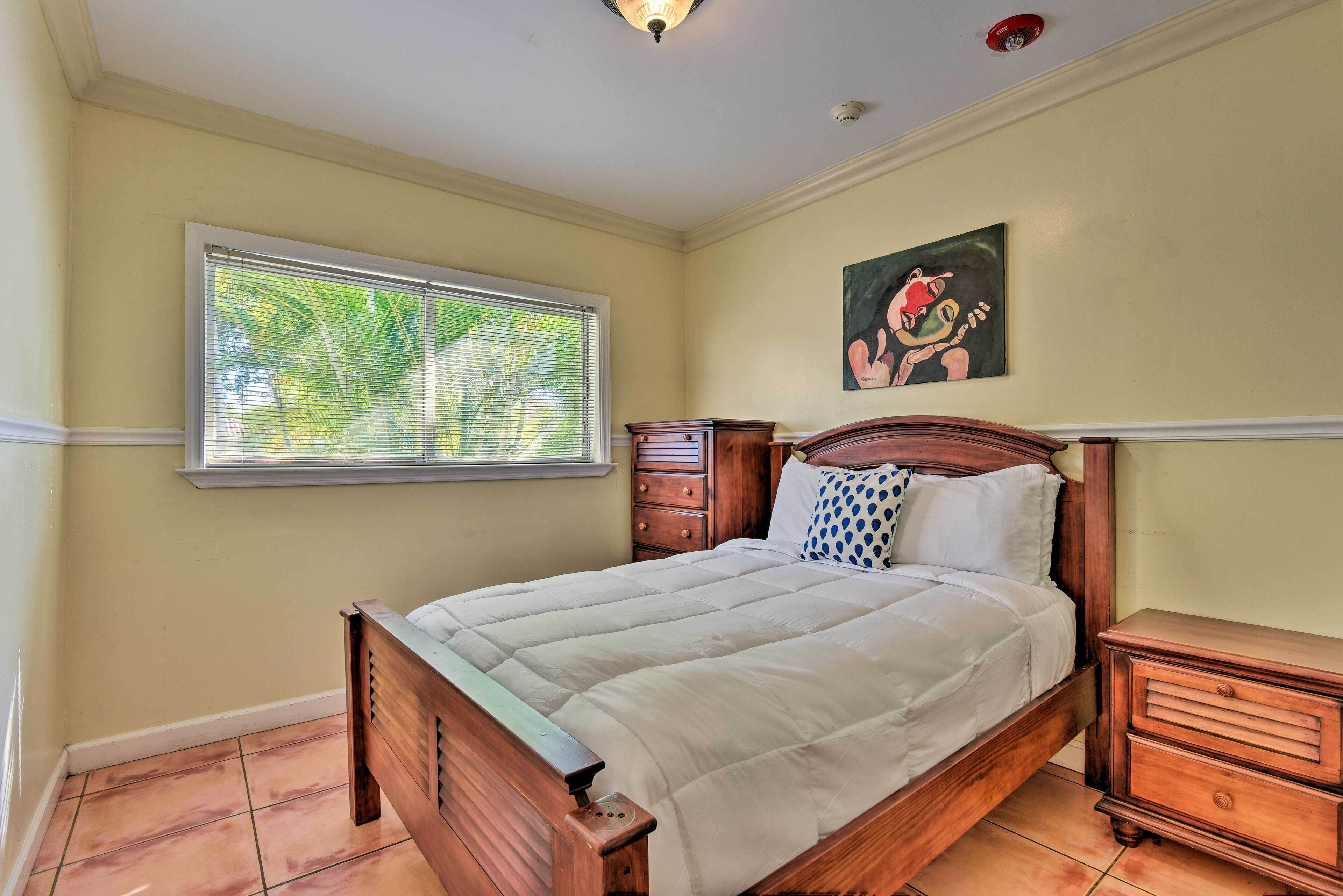 Une chambre à coucher avec un lit en bois, une table de chevet, une commode, une fenêtre avec des stores et un tableau accroché au mur.