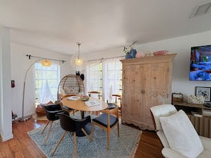 A dining area with a round table, chairs, a wooden cabinet, and a television on the wall.