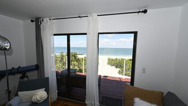 A room with a large window overlooking a beach, a telescope, and a cozy seating area. - Beachfront 2BR North Captiva Cottage with Private Beach (North Captiva)
