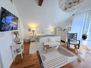 A bedroom with a bed, bedside tables, a TV, a chair, and a window.