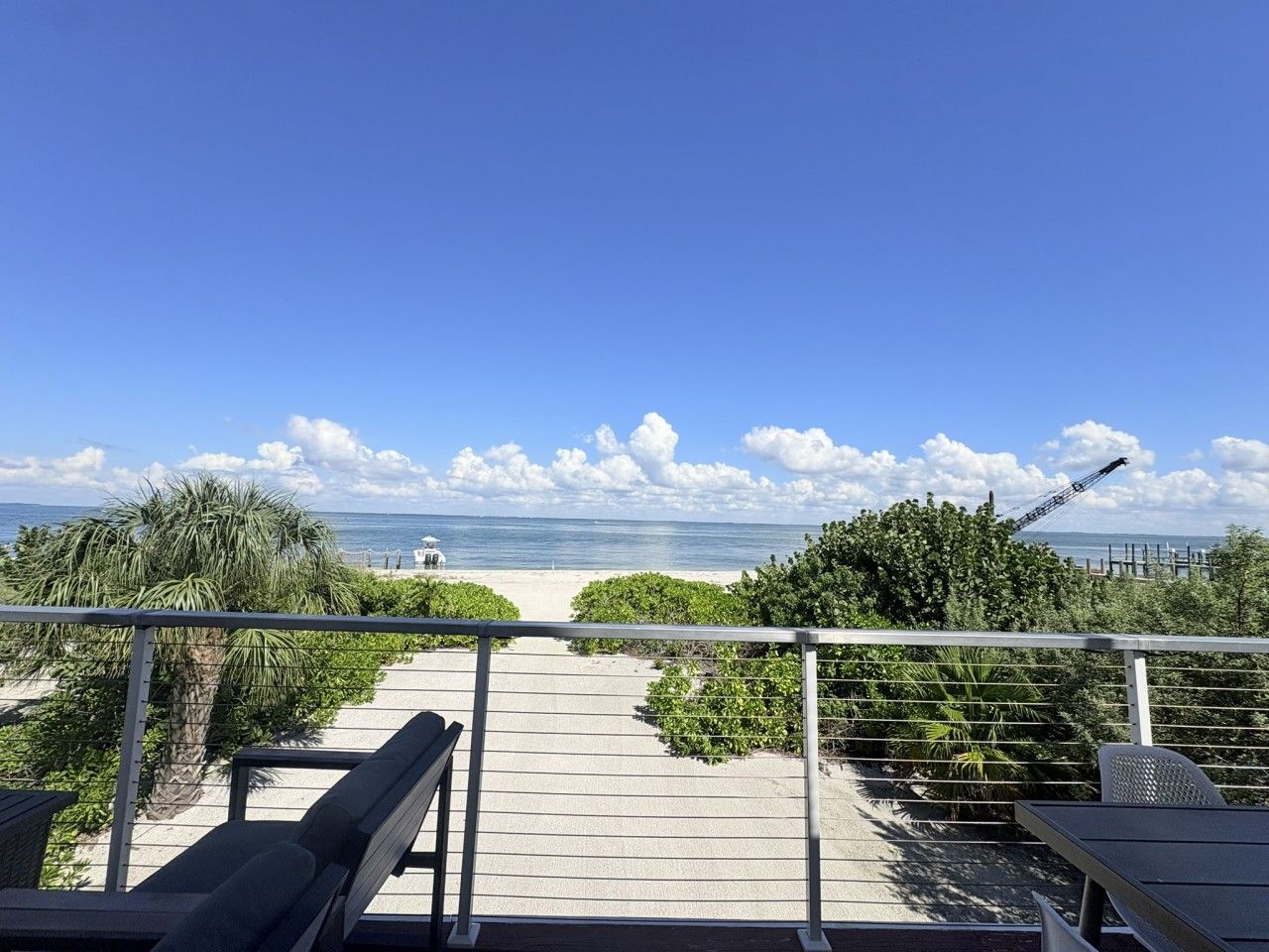 A balcony with a view of the beach and ocean, a palm tree, and a crane in the distance.