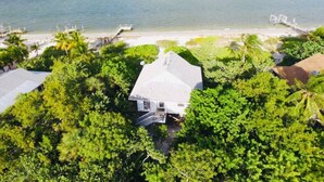 An aerial view of a house surrounded by lush greenery, with a view of the ocean and a dock extending into the water. - Beachfront 2BR North Captiva Cottage with Private Beach (North Captiva)
