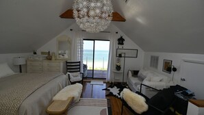 A bedroom with a large bed, a desk, a chair, a lamp, and a view of the sea through a sliding door. - Beachfront 2BR North Captiva Cottage with Private Beach (North Captiva)