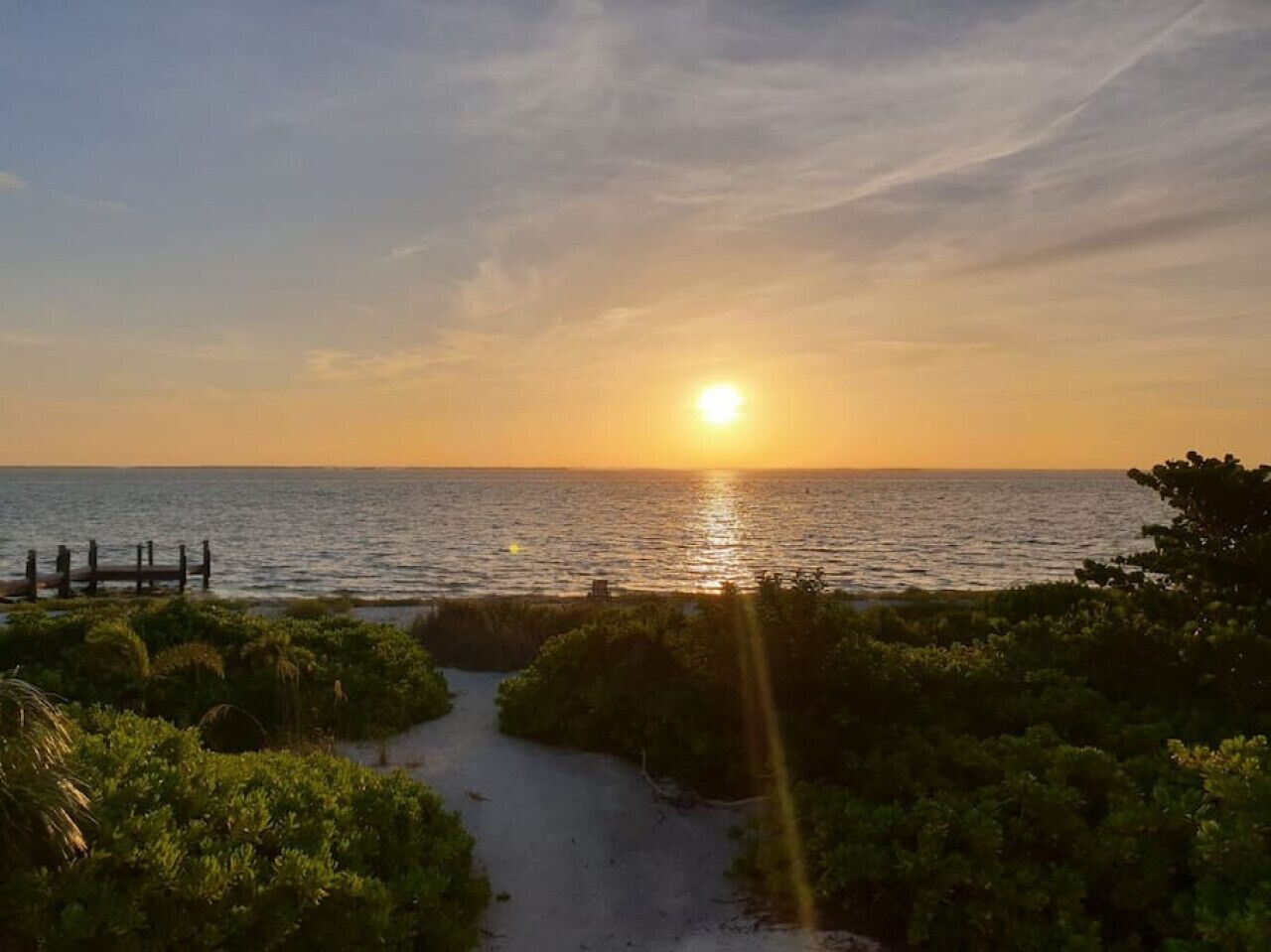 A sunset view over a beach with a wooden walkway leading to the water.