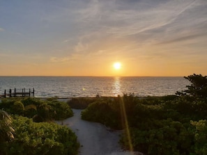 A sunset view over a beach with a wooden walkway leading to the water.