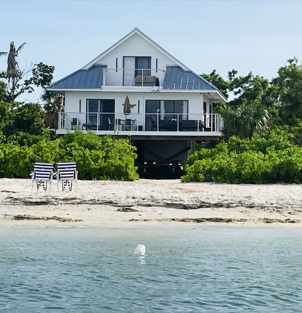 A beachfront house with a balcony, two chairs, and a view of the sea.